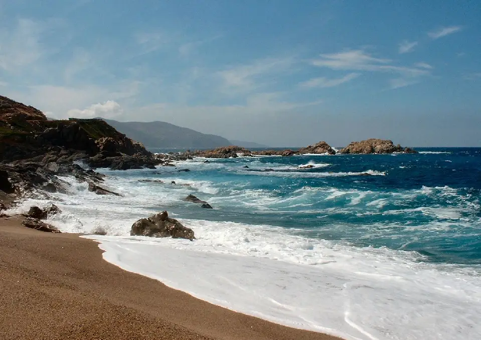 A beach with waves crashing on it and rocks in the background.