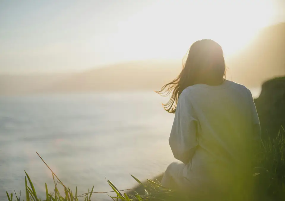 A woman sitting on the beach looking out at the ocean.