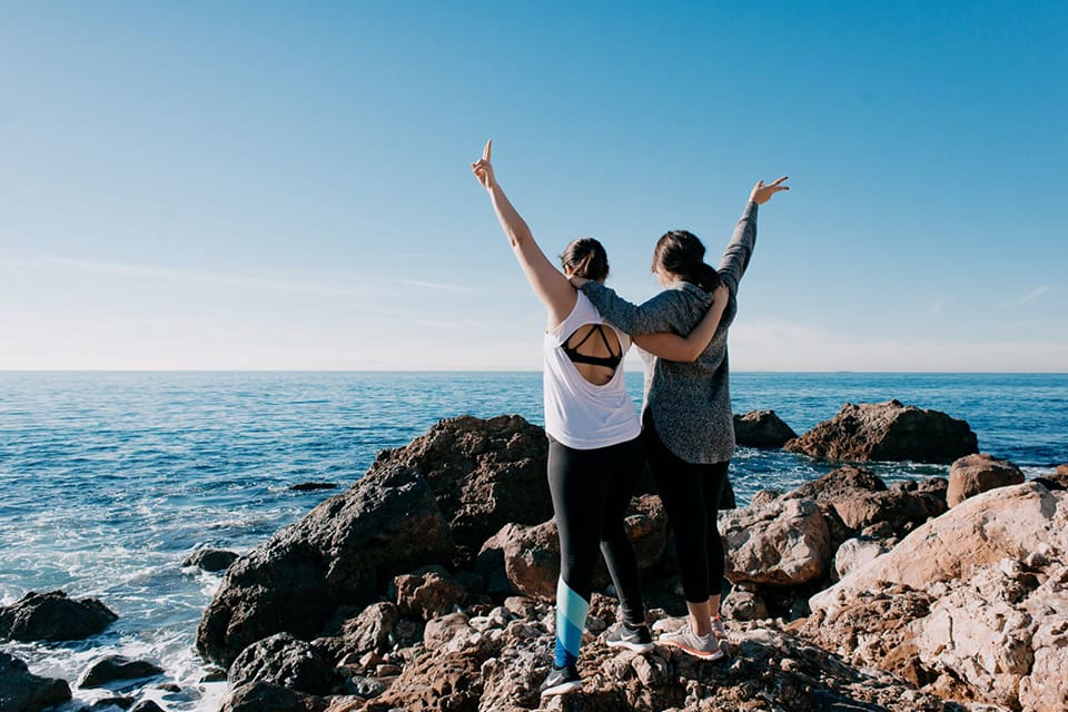 Two people standing on a rock near the ocean.