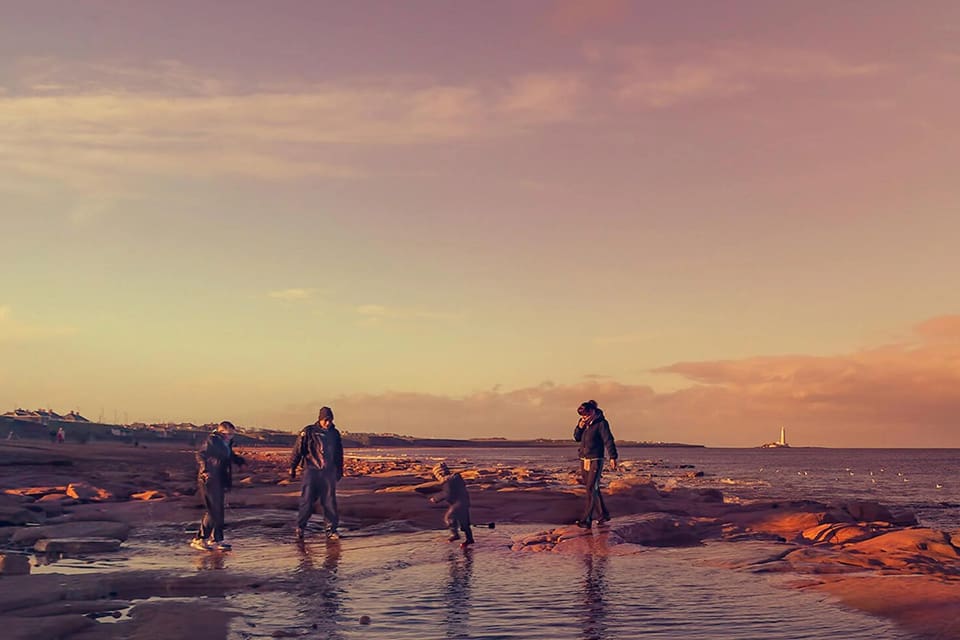 A group of people walking in the water at sunset.