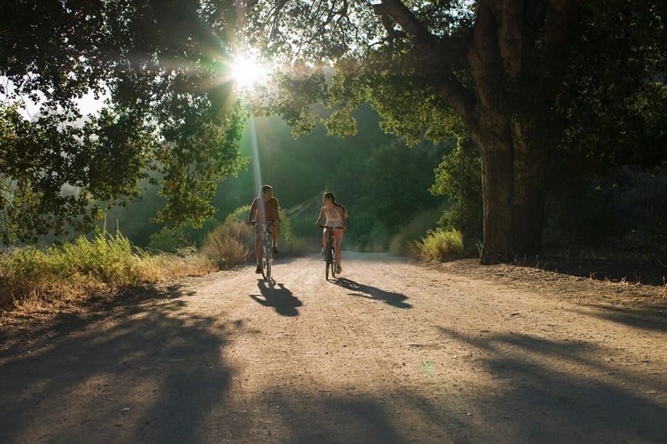 Two people riding skateboards on a dirt road.