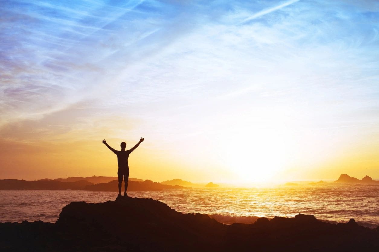 A person standing on top of a rock near the ocean.